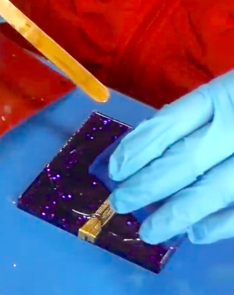 Pouring another layer of resin on the homemade Christmas present to seal the gold ribbon