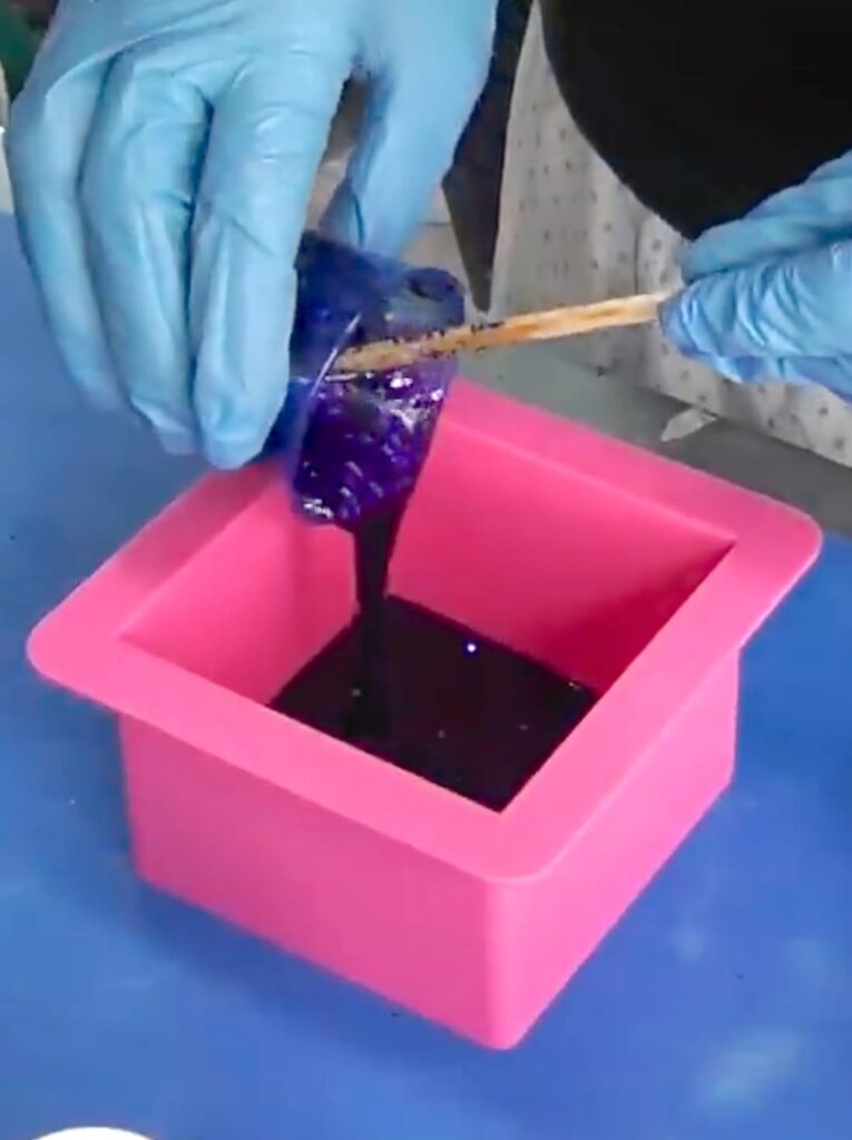 Pouring purple glitter resin into a pink square coaster mold