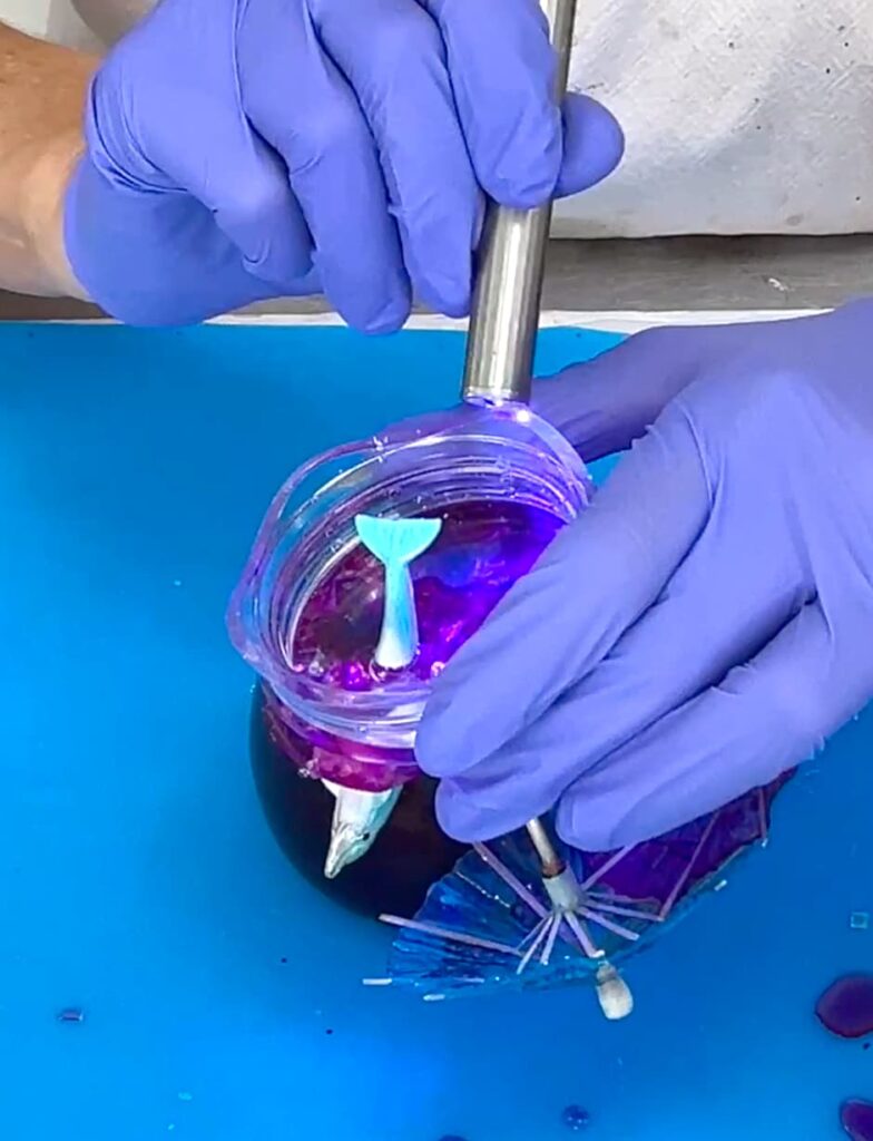 Using UV resin to attach the tail of the dolphin to the bottom of the jar lid