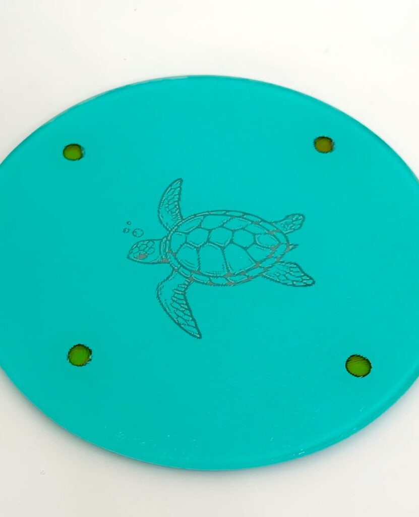 Round glass cutting board laser engraved with a turtle but has four round dots