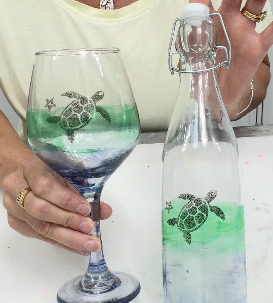 doing glass painting on a wine glass with a paintbrush and green paint
