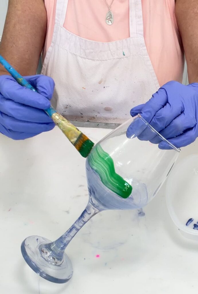 doing glass painting on a wine glass with a paintbrush and green paint