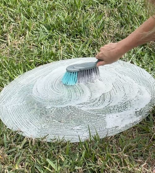 Scrubbing round glass table top with soap and a brush
