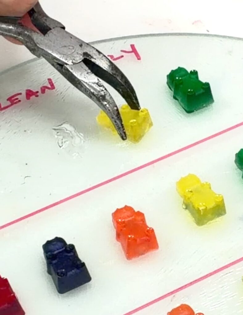 Using pliers to determine which glue sticks to glass best by pulling off a yellow gummy bear