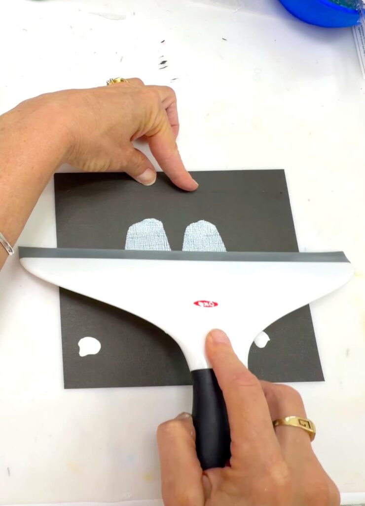 Easy paint idea pulling a squeegee and smearing white paint into the shape of a ghost